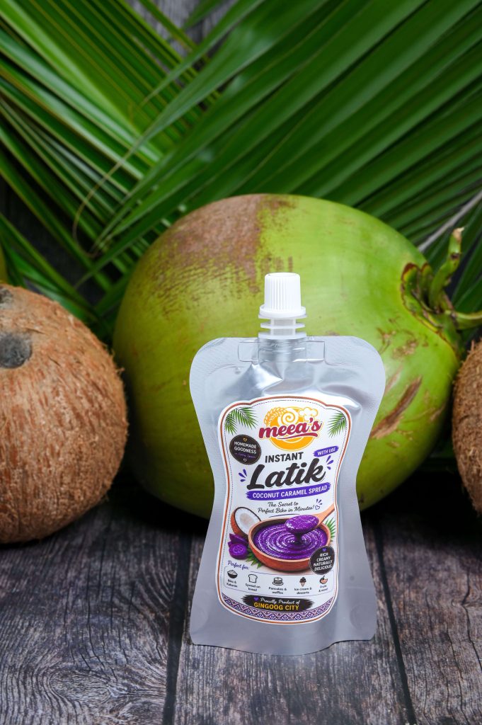 Armand Ansaldo Photography UntiSingle pouch of Meea's Instant Latik Coconut Caramel Spread centered between whole coconuts on a rustic wooden tabletled 0000 207