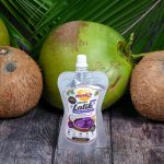 Single pouch of Meea's Instant Latik Coconut Caramel Spread centered between whole coconuts on a rustic wooden table